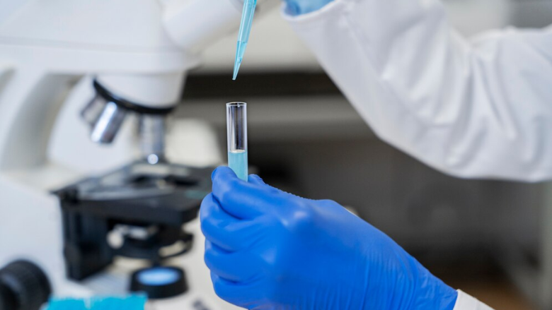 scientist holding pipe and pipette microscope in background