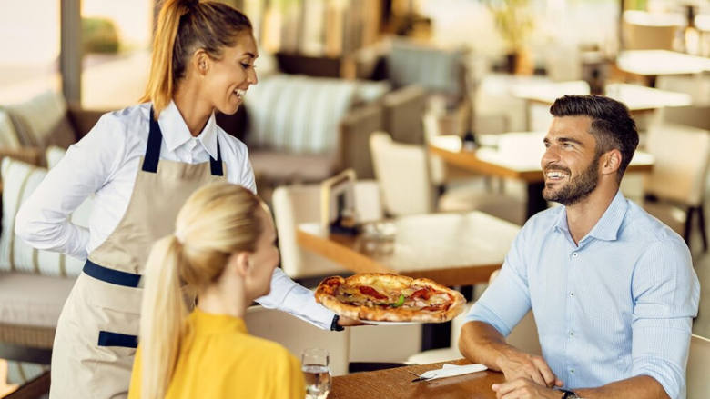 waitress serving pizza to couple at restaurant