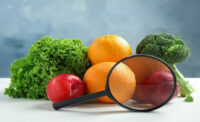 Fresh fruits, vegetables and magnifying glass on white table against light blue background. Food poisoning concept