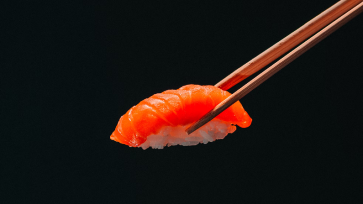 Salmon sushi with rice hold with chopsticks on black background