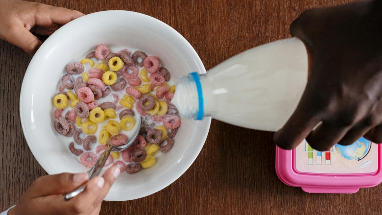an adult's hand pouring milk into a child's cereal bowl