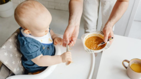 baby in high schair offered bowl of mushy orange food