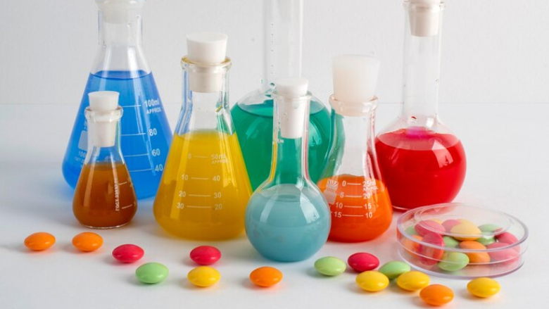 beakers containing multicolored liquids next to colorful candies