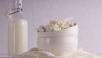 bowl of cottage cheese with a spoon next to glass jar of milk