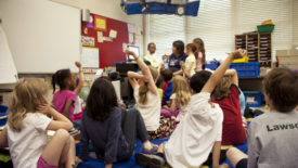 children sitting on rug hands raised at preschool during reading time