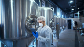 factory worker with tablet next to tanks of liquid dairy