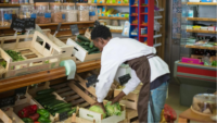 grocer bent over fixing vegetable display