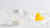 half full baby bottle next to rubber duckie on white surface