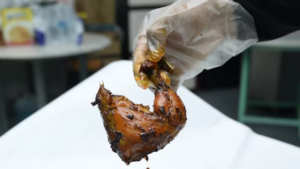 hand wearing foodservice glove holding charred chicken thigh