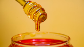 honey wand dripping over honey jar yellow background