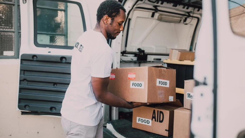 person putting boxes labeled food, aid, medicine in back of van