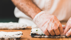 person wearing plastic gloves making sushi