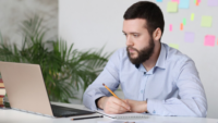 professional person looking at laptop while taking notes