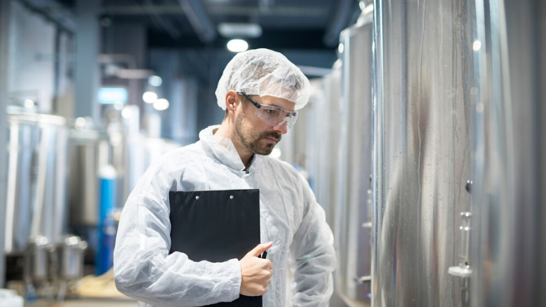 technician looking thoughtful next to dairy tanks in processing plant