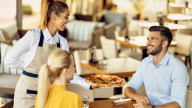 waitress serving pizza to couple at restaurant