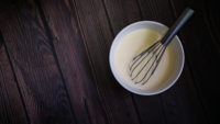 whisk in a bowl of pancake batter on a dark wooden table