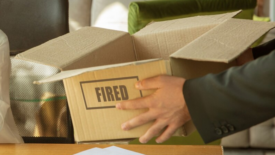 businessman holding cardboard box that says FIRED on it