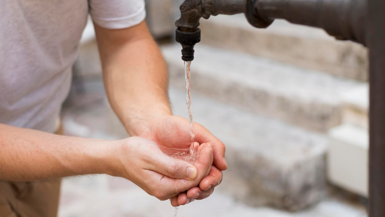 man cupping hands beneath running water from outdoor pump