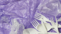 plastic cutlery and clear plastic film on purple background