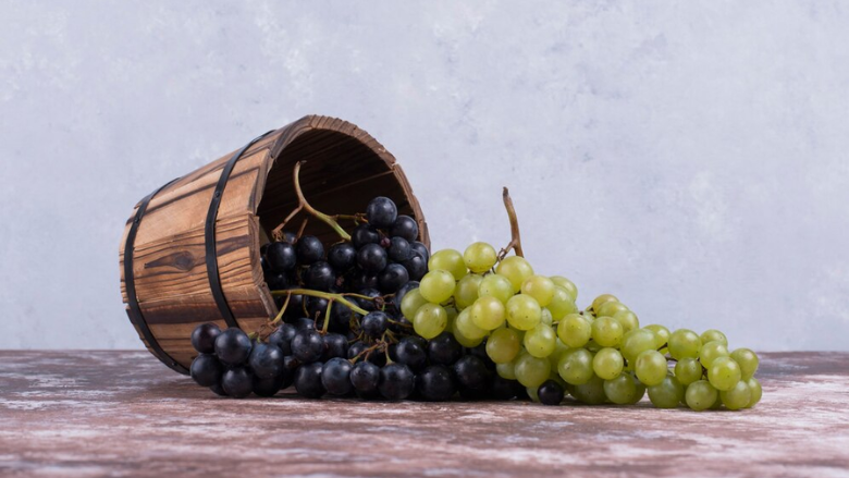 red and green grapes spilling out of overturned wooden bucket