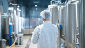 technologist in ppe walking through dairy processing factory