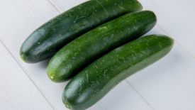 three whole cucumbers on white wood surface