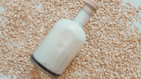 glass bottle of oat milk lying on bed of rolled oats