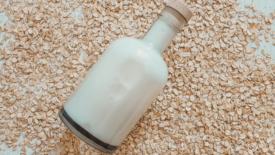 glass bottle of oat milk lying on bed of rolled oats