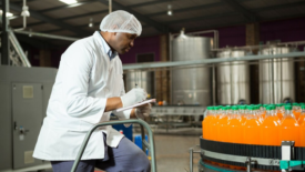 auditor with clipboard looking at soda bottles on production line